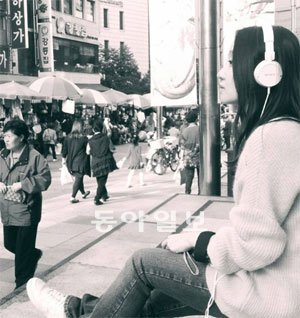 한 관객(헤드폰을 착용한 여성)이 남대문시장 입구 계단에 앉아 바삐 오가는 인파를 바라보며 ‘군중 속의 고독’을 음미하고 있다. 한국공연예술센터 제공
