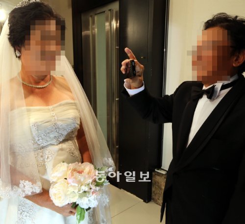 13일 서울 강남구 청담동의 한 웨딩숍에서 정병두 씨(오른쪽)가 웨딩드레스를 입은 신부 김월례 씨의 모습을 휴대전화로 찍으며 환하게 웃고 있다. 정 씨 부부는 한센인에 대한 편견을 이기기 위해 공개 결혼식을 결심했지만 언론에 얼굴을 공개하는 것은 꺼려 모자이크 처리했다. 김경제 기자 kjk5873@donga.com