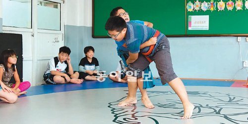 모래 대신 매트 위에서 씨름을 즐기는 어린이들. 바닥에는 조선시대 풍속화가 김홍도의 씨름도가 그려져 있다. 국민생활체육회는 간편하게 설치할 수 있는 씨름 전용 매트를 전국의 초등학교에 보급하고 있다. 국민생활체육회 제공