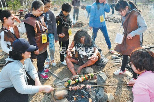 경기 연천군 전곡선사박물관의 1박 2일 프로그램 참가자들이 원시인 복장을 한 채 나무꼬치에 끼운 고기를 구워 먹고 있다. 경기문화재단 제공