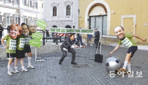 독일 프랑스 이탈리아 스페인 4개국 정상회의가 열린 2012년 6월 22일 이탈리아 로마에서 시위대가 각 정상의 얼굴이 그려진 마스크를 쓰고 퍼포먼스를 벌이고 있다. 앙겔라 메르켈 독일 총리, 마리아노 라호이 스페인 총리, 마리오 몬티 이탈리아 총리(왼쪽부터)가 ‘금융거래세’라고 쓰인 골대 옆을 지키는 가운데 ‘로빈후드팀’을 표방하는 프랑수아 올랑드 프랑스 대통령의 마스크를 쓴 시위대원(오른쪽)이 골을 넣으려는 동작을 하고 있다. 동아일보DB