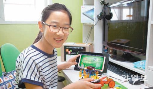 LG 사랑의 다문화학교 스마트 클래스에 참여하는 장채원 양이 경기 안산의 자기집 방에서 태블릿 PC와 그동안 만든 조립물들을 모아놓고 미소를 짓고 있다. LG그룹 제공