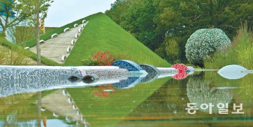 프랑스 롱르소니에 시에 영구 보존되는 황지해 작가의 정원 ‘뻘: 순천만, 어머니의 손바느질’. 흙을 채운 철골 구조물에 흰 꽃을 동그랗게 심은 플라워 돔(오른쪽)과 푸른 언덕이 수심 1cm 위 계류에 비쳐 장관을 이룬다. 이성용 씨 제공