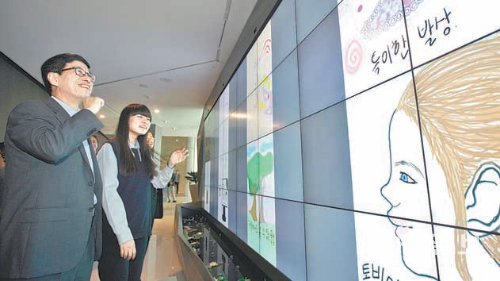 하성민 SK텔레콤 사장(왼쪽)이 26일 서울 중구 을지로 SK텔레콤 본사 2층 정보통신기술(ICT) 체험관 ‘티움’에서 학생들이 태블릿PC로 그린 그림을 감상하고 있다. SK텔레콤 제공