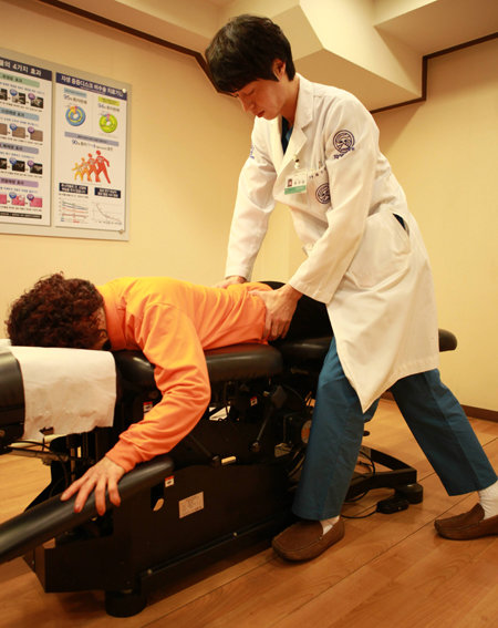 추나요법 시술 장면. 추나요법에 필요한 특수 장비 위에서 한의사가 손과 몸을 활용해 틀어진 척추를 바로잡는다.