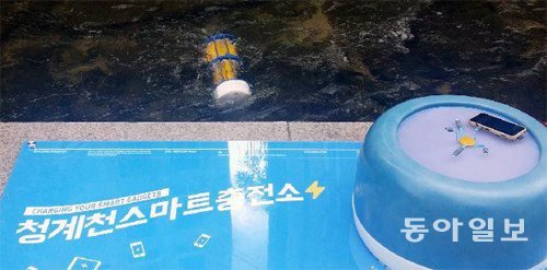 서울 청계천 광통교 인근에 흐르는 물속에 소형 수력발전기(위)를 넣어 스마트폰을 무료로 충전할 수 있는 ‘청계천스마트충전소’가 27일 설치됐다. 황인찬 기자 hic@donga.com