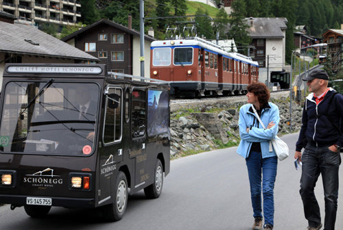 체르마트 마을길로 전기차가 지나는 모습. 뒤로 고르너그라트 산악열차가 보인다.