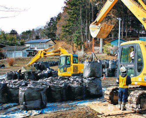 ‘검정 비닐백’ 천지 후쿠시마 현 이타테 촌에서 인부들이 굴착기로 오염토가 담긴 검정 비닐백을 옮기고 있다. 비닐백은 이타테 촌의 논밭에 놓여 있는데, 전체 농지 800ha(1ha는 1만 m²) 중 약 3분의 1을 덮고 있다. 후쿠시마=박형준 특파원 lovesong@donga.com