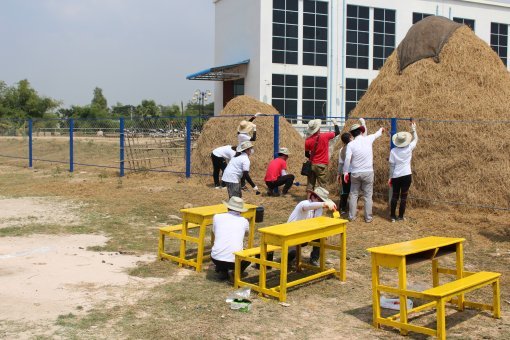 캄퐁참마을의 초등학교에서 낡은 울타리와 책상을 페인트로 깨끗이 칠하고 있는 새마을국제개발학과 학생들. 새마을운동 결과 1년에 한차례 수확하던 벼를 두세차례 수확하게 된 것을 기념하듯 운동장에 놓인 볏짚단이 눈에 띈다.