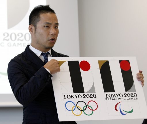 FILE - In this Aug. 5, 2015, file photo, Japanese designer Kenjiro Sano gives a detailed explanation of how he came up with his logo, left, for the 2020 Tokyo Olympics at a press conference in Tokyo. Tokyo Olympic organizers defended Sano in a logo scandal Friday, Aug. 28, 2015, denying allegation his design for the 2020 Games was taken from a Belgian theater. The organizers disclosed Sano？ initially submitted logo, saying its emphasis on ？?shape had no resemblance to that of Theater de Liege and that a circle on the background was added later when his design was touched up. (AP Photo/Ken Aragaki, File)