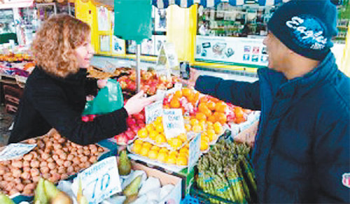 영국의 과일가게에서 한 이민자(오른쪽)가 과일을 구입할 때 필요한 영어 대화 내용이 제공되는 스마트폰을 보면서 과일을 사고 있다. 배재대 제공