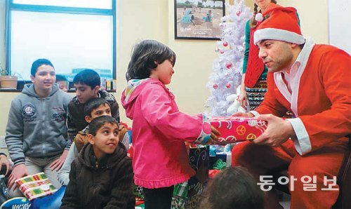 23일 산타클로스 복장을 한 미국 뉴저지 난민정착지원센터의 마무드 마무드 국장이 난민 어린이에게 크리스마스 선물을 주고 있다. 아이들이 행복해하는 표정이다. 뉴욕=부형권 특파원 bookum90@donga.com