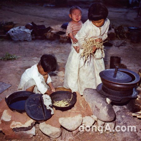 피난민촌 아이들. 남동생을 업고 식사준비를 하는 누나. 솥에 쌀 대신 마른 풀만 가득하다.