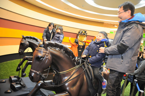 렛츠런파크 서울 ‘시크릿 웨이 투어’의 세 번째 코스인 ‘놀라운지’에서 한 가족 체험객들이 4D기기를 이용한 기수체험을 하고 있다. 렛츠런파크 서울의 명소를 체험하는 ‘시크릿 웨이 투어’가 최근 가족 및 연인들의 데이트 코스로 인기를 끌고 있다. 사진제공｜한국마사회