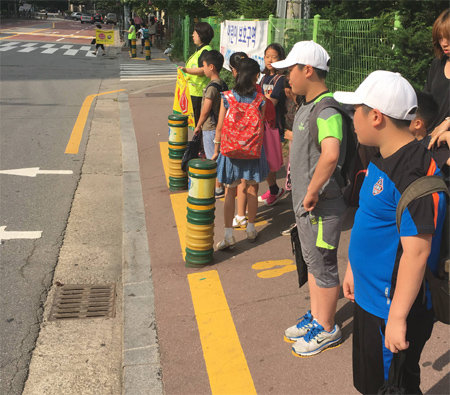 노란 발자국이 처음 시행된 경기 용인시 상현초등학교 앞 등교 시간대 학생들 모습. 모두 노란 정지선 밖의 발자국 위에서 나란히 신호를 기다리고 있다. 경기남부지방경찰청 제공