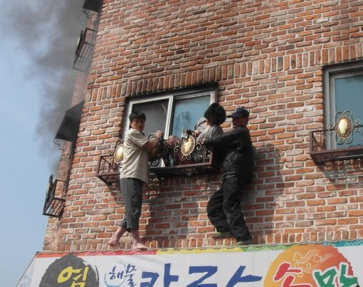 15일 충북 청주시 서원구 다세대주택 화재 현장에서 용감한 이웃 2명이 부상당한 여성을 붙잡은 채 119구조대가 오기를 기다리고 있다. 왼쪽이 김기운 씨고 오른쪽 이웃은 신원이 알려지지 않았다. 청주서부소방서 제공