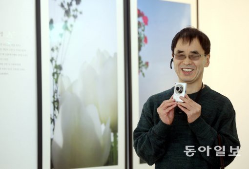 시각장애인 김경식 씨가 6년간 써온 자신의 디지털카메라를 들고 사진을 찍으며 활짝 웃고 있다. 김 씨의 뒤로 그가 찍은 사진들이 걸려있다. 박영대 기자  sannae@donga.com