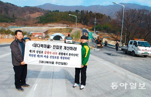 4일 오전 부산항 신항 제2배후도로의 굴암터널 입구에서 대장마을(대다복마을) 주민 정봉용 씨(오른쪽)와 김진도 씨가 자신들의 요구사항이 담긴 현수막을 펼쳐 보이고 있다. 정 씨 오른쪽이 대장마을, 김 씨 뒤쪽 멀리 보이는 곳이 대다복마을이다. 강정훈 기자 manman@donga.com