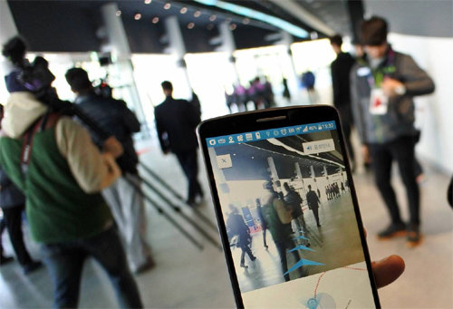 평창동계올림픽조직위원회 관계자가 16일 강원 강릉 아이스아레나 실내에서 ‘증강현실(AR) 길 찾기’ 기능을 시연하고 있다. 
스마트폰 화면에 비친 실제 모습 위로 AR를 통해 특정 좌석으로 가는 길이 화살표로 안내되고 있다. 미래창조과학부 제공