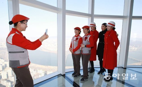 서울 송파구 롯데월드타워 단지 안에서 일하는 파트너사 직원들이 28일 롯데월드타워 118층에 설치된 유리 전망대 ‘스카이데크’에 올라서 기념사진을 찍고 있다. 롯데물산 제공