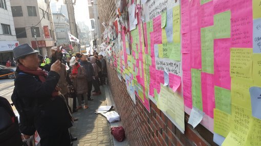 박근혜 전 대통령 사저 앞에서 집회 중인 사람들. 일부 참가자가 포스트잇 내용을 촬영하고 있다.