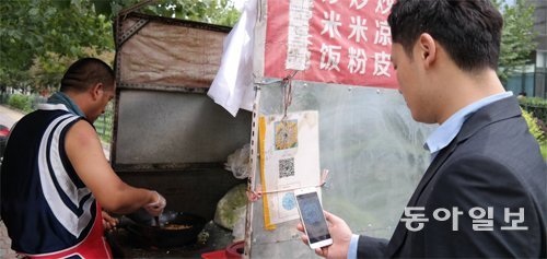 정동연 채널A 특파원(오른쪽)이 24일 오후 베이징 거리의 한 노점에서 중국의 대표적 길거리 음식인 20위안(약 3300원)짜리 
차오빙(볶음 밀전병)을 산 뒤 노점에 붙은 QR코드를 이용해 모바일 결제를 하고 있다. 베이징=윤완준 특파원 
zeitung@donga.com