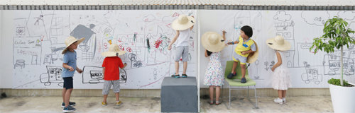 ‘동네드로잉-상상의 정원’이 설치된 옥상에서 밀짚모자를 눌러쓴 어린이들이 작품에 색을 입히고 덧그림을 그려 새로운 동네 모습을 완성하고 있다. <헬로우뮤지움>