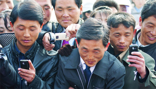 휴대전화로 사진 찍는 북한 주민들. 요금을 내기 어려워 기기만 갖고 다니는 사람들이 많아 휴대전화는 ‘비싼 손전등’으로 불리기도 한다. 정전이 자주 일어나는 북한에서 전기가 나가면 휴대전화를 꺼내드는 게 유행처럼 번졌기 때문이다. ⓒJoseph A Ferris Ⅲ