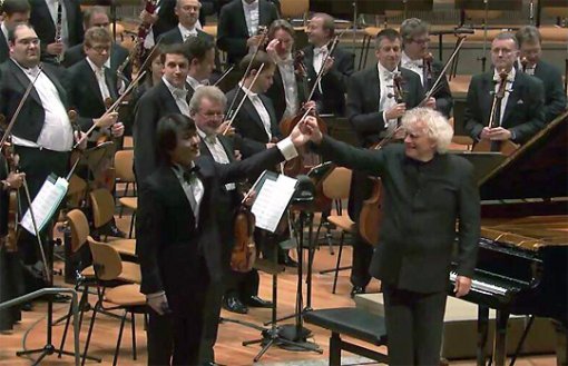 피아니스트 조성진(왼쪽)이 4일(현지 시간) 독일 베를린에서 베를린 필하모닉과의 첫 협연 무대 뒤 지휘자 사이먼 래틀의 손을 잡고 관객에게 인사하고 있다. 베를린필하모닉과의 협연은 조성진의 음악적 꿈 중 하나였다. 베를린 필하모닉 인터넷 생중계 캡처
