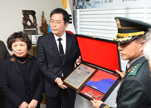이학기 국방부 유해발굴감식단장(오른쪽)이 30일 고 김재권 일병의 아들 김성택 씨 자택에서 열린 ‘호국의 영웅 귀환행사’에서 김 씨에게 ‘호국의 얼 함’을 전달하고 있다. 국방부 제공