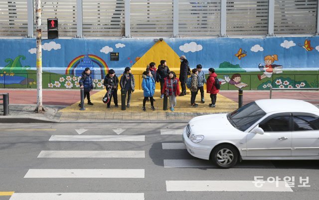 서울 시내 한 어린이 보호구역(스쿨존)에 마련된 ‘옐로카펫’ 위에서 어린이들이 횡단보도 보행신호를 기다리고 있다. 옐로카펫은 어린이들이 보행신호를 안전하게 기다리도록 한 아이디어 디자인이다. 옐로카펫 등 어린이 교통안전 사업 정책 확대에 힘입어 지난해 어린이 교통사고 사망자 수는 2016년보다 23.9% 줄어든 54명을 기록했다. 동아일보DB