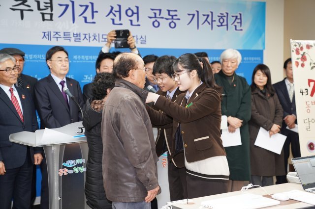 제주시 애월고교 학생들이 4·3사건의 의미를 되새기기 위해 자체 디자인해 제작한 동백꽃 배지를 생존희생자에게 달아주고 있다. 제주도 제공