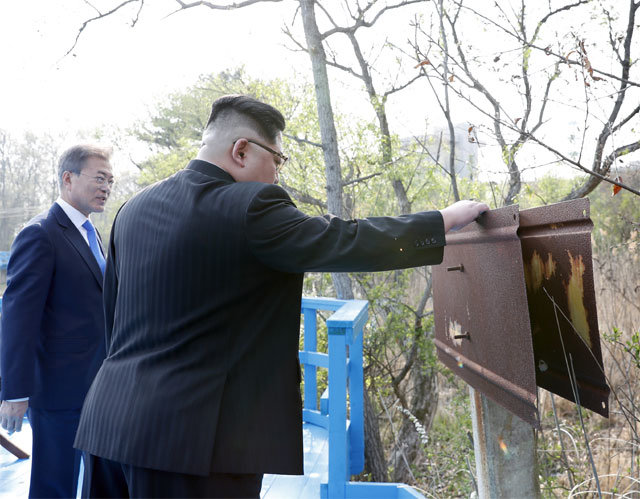 녹슨 군사분계선 표지판 김정은 북한 국무위원장이 27일 판문점 ‘도보다리’ 옆 군사분계선 표지판을 만져보고 있다. 임진강에서 동해까지 1292개의 표지판 중 101번째인 이곳에는 ‘0101’이라는 숫자가 있었으나 지금은 녹슬어 잘 보이지 않는다. 판문점=한국사진공동취재단