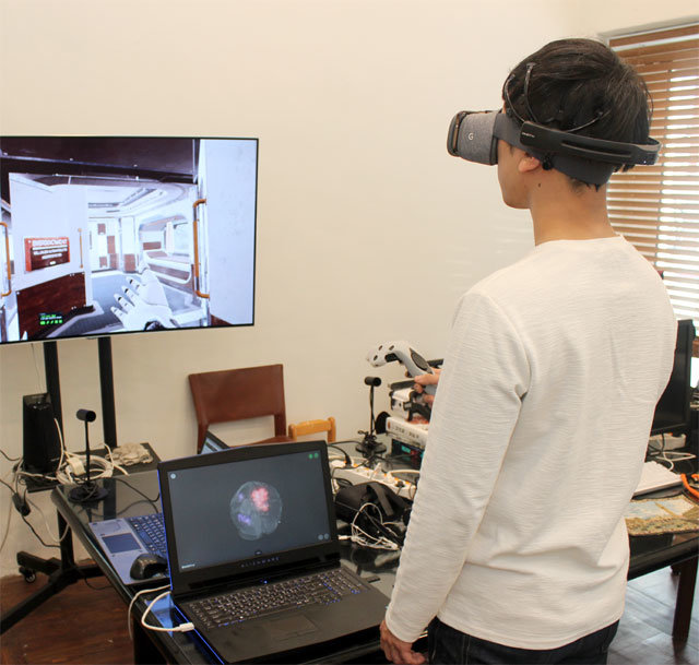 한 연구원이 가상현실(VR) 기기와 휴대용 뇌전도(EEG) 기기를 착용한 채 가상 공간을 거닐고 있다. 노트북 모니터에는 뇌파가 기록되고 있다.