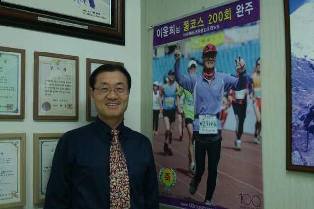 이윤희 대표가 서울 성수동 사무실에서 풀코스 200회 완주(2016년 동아마라톤) 기념 사진을 배경으로 포즈를 취했다.