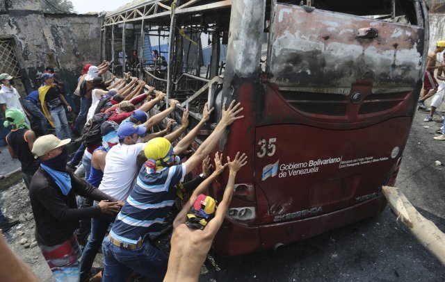 23일(현지시간)베네수엘라 우레나에서 시민과 군이 충돌한 가운데 시위대가 불에 탄 버스를 밀어내고 있다. 우레나=AP/뉴시스