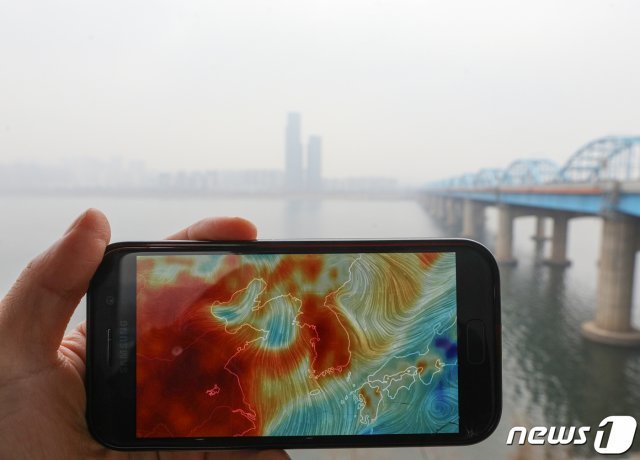 초미세먼지 주의보가 발령된 25일 오전 서울 동작대교에서 바라본 도심이 뿌옇게 보인다. 왼쪽 스마트폰 화면은 미국 국립기상청의 데이터를 기반으로 지표면의 기상 상황을 나타내는 사이트(earth.nullschool.net)에 나타난 붉은 초미세먼지(PM2.5) 표시가 한반도를 뒤덮고 있는 모습. 2019.2.25/뉴스1 © News1