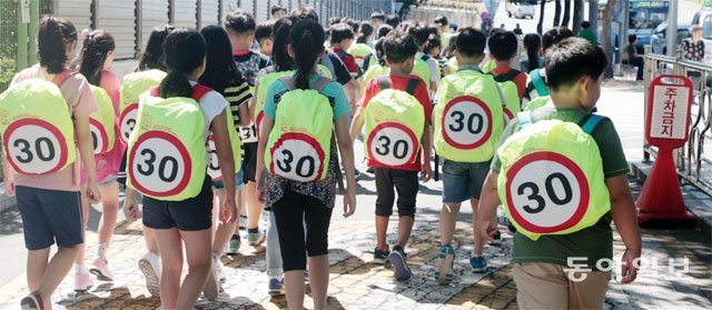 부산시교육청이 지난해 관내 초등학교에 보급한 ‘안전덮개’를 가방에 씌운 어린이들이 보도를 걷고 있다. 덮개에 쓰인 숫자 ‘30’은 어린이보호구역(스쿨존) 내 제한 최고속도인 시속 30km를 의미한다. 어린이들을 움직이는 속도 표지판으로 활용한 것이다. 동아일보DB