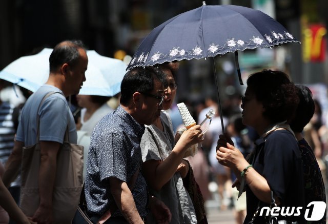 서울의 낮 최고기온이 31도까지 오르며 무더운 날씨를 보인 23일 오후 서울 명동거리에서 관광객들이 우산을 들고 아이스크림을 먹으며 더위를 피하고 있다. 2019.6.23/뉴스1 © News1