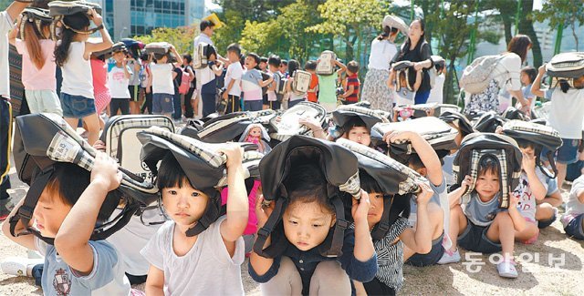 지진 대피훈련에 참여한 유치원생들이 학교 운동장으로 대피한 뒤 가방을 들어올려 머리를 보호하고 있다. 반복적인 안전훈련은 실제 재난 상황에서의 침착한 대피로 이어진다. 동아일보DB