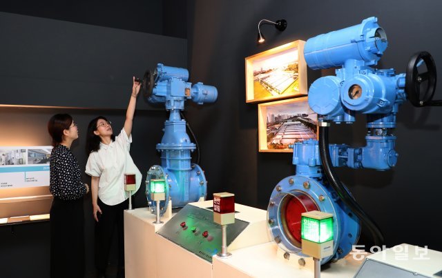 수도박물관 전시회를 방문한 관람객들이 수도 펌프 배수 장치의 작동 원리를 살펴보고 있다.