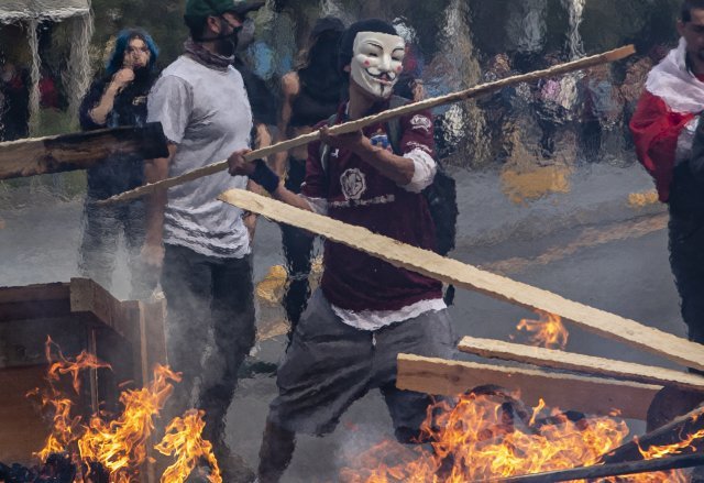 지난 19일 칠레 산티아고에서 시위대들이 불타는 바리케이드에 목재를 집어넣고 있다. [산티아고=AP/뉴시스]