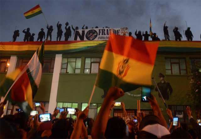 8일 볼리비아 정부에 항명을 선언하고 반정부 시위에 가세한 코차밤바 지역 경찰들이 이곳 경찰청 옥상에 올라가 헬멧과 검은 마스크를 쓴 채 국기를 흔들고 있다. 코차밤바=AP 뉴시스