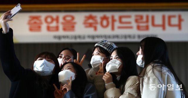 졸업생과 친구들이 행사가 열릴 예정이었던 대강당에서 마스크를 쓰고 기념 사진을 찍고 있다.