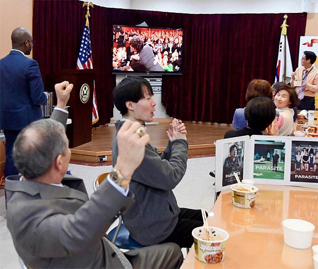 해리 해리스 주한 미국대사(왼쪽)가 10일 서울 종로구 주한 미국대사관에서 직원들과 ‘짜파구리’를 먹으며 아카데미 시상식을 시청하던 중 ‘기생충’ 작품상 수상 소식에 두 팔을 들며 환호하고 있다. 주한미국대사관 제공