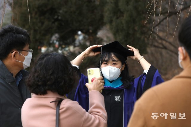 마스크를 쓴 졸업생이 기념 사진을 찍기 전 모자를 쓰고 있습니다.