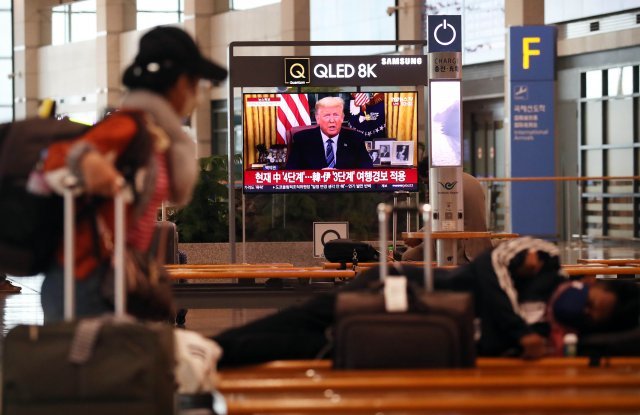 미국 트럼프 대통령이 코로나19 관련 대국민 연설을 한 12일 오전 인천국제공항 입국장에서 여행객들이 생중계를 지켜보고 있다.