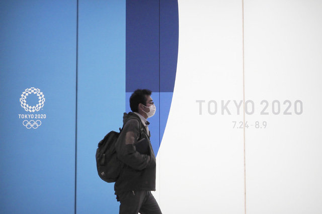 일본 도쿄 시내에서 마스크를 쓴 시민이 2020 도쿄 올림픽 홍보문구 앞을 지나고 있다. 코로나19의 세계적인 확산으로 7월 도쿄 올림픽이 예정대로 열릴지는 점점 불투명해지고 있다. 도쿄=AP 뉴시스