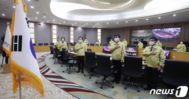 정세균 국무총리와 국무위원들이 24일 정부세종청사 국무조정실 국무회의장에서 열린 서울-세종 영상 국무회의에서 국민의례를 하고 있다. 이날 회의에는 각 부처 장·차관들이 사회적 거리두기 일환으로 의자 한칸 씩 비워 거리를 두고 앉았다. © News1