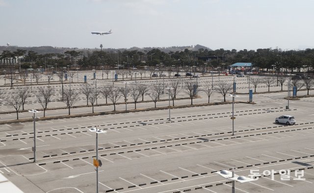 공항 주차장이 텅 비어있는 가운데 뒤편으로 항공기가 착륙하고 있다.